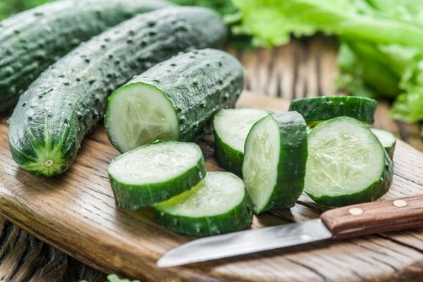 Partially cut cucumber on a cutting board with a paring knife beside it.